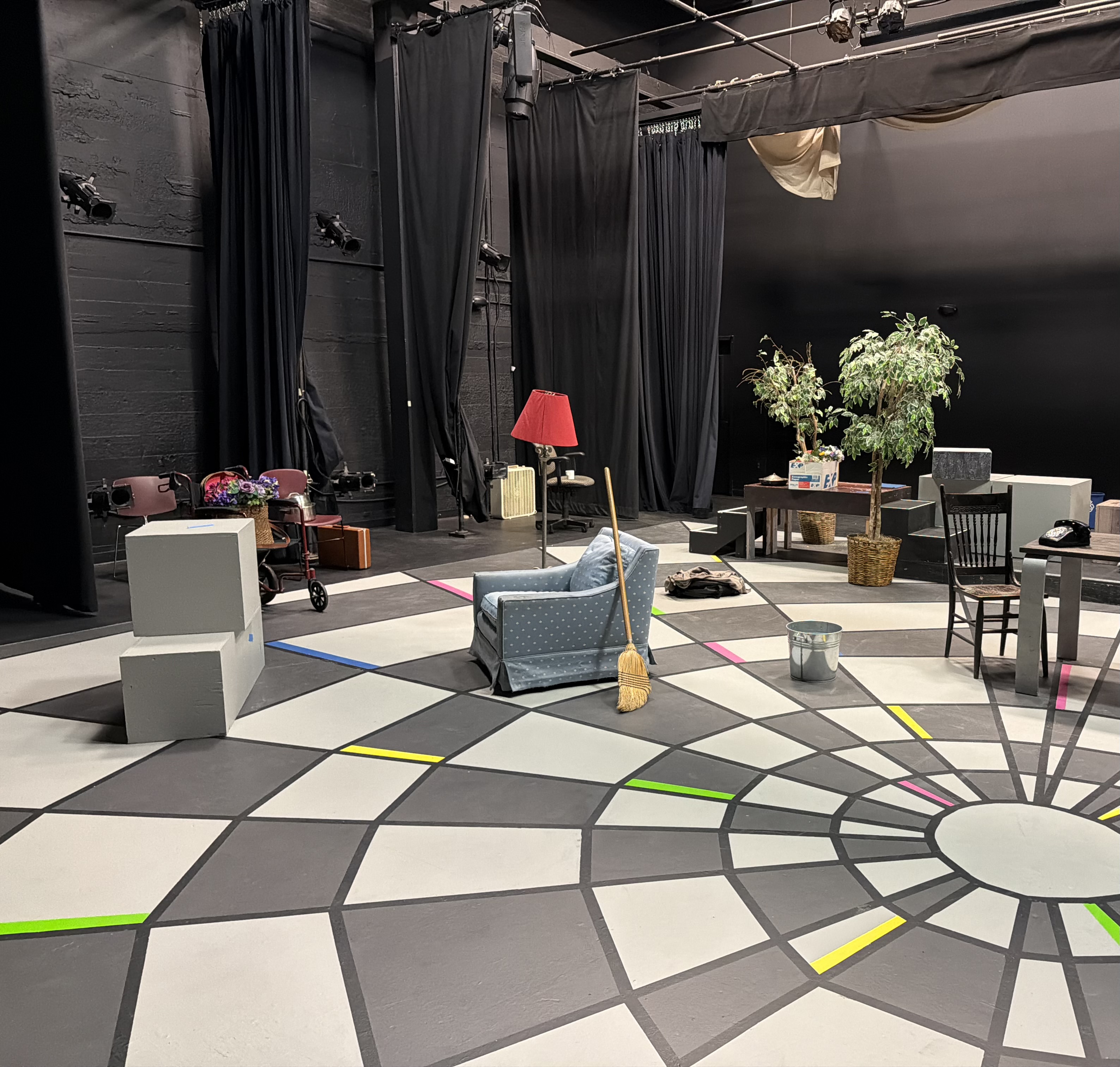 An armchair, lamp, broom, telephone, and other props arranged onstage